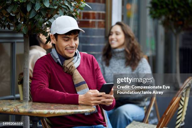 man texting on phone at cafe - man wearing baseball cap stock pictures, royalty-free photos & images