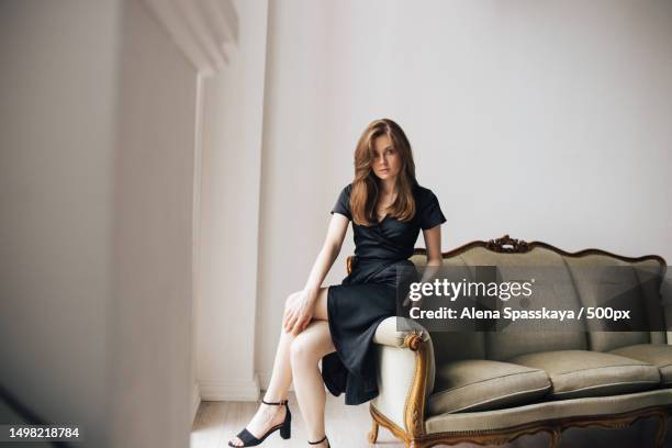 young girl in a black dress sits on a sofa in a photo studio,russia - black dress stock pictures, royalty-free photos & images