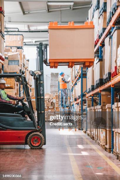 uniformed worker driving and loading cardboard boxes with forklift stacker loader in a factory warehouse - forklift truck stock pictures, royalty-free photos & images
