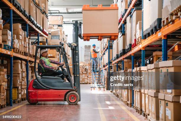 trabajador uniformado conduciendo y cargando cajas de cartón con cargador apilador de carretilla elevadora en un almacén de fábrica - unloading fotografías e imágenes de stock