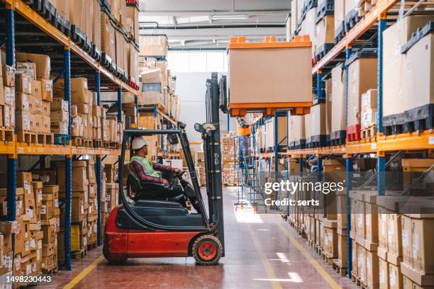 trabajador uniformado conduciendo y cargando cajas de cartón con cargador apilador de carretilla elevadora en un almacén de fábrica - carretilla elevadora fotografías e imágenes de stock