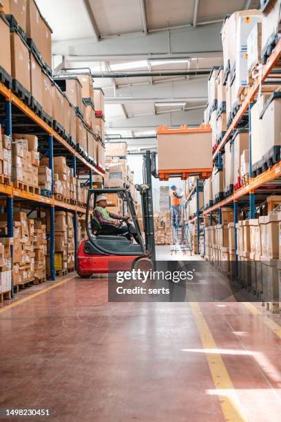 uniformed worker driving and loading cardboard boxes with forklift stacker loader in a factory warehouse - man lifting truck stock pictures, royalty-free photos & images