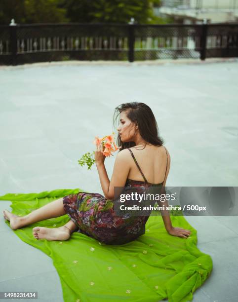 woman holding flower while sitting on concrete floor and green blanket,india - hair editorial stock pictures, royalty-free photos & images