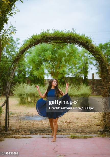 portrait of smiling young woman dancing in blue dress against garden,india - photoshop photos et images de collection