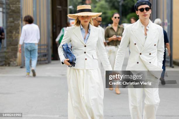 Couple wears straw hat, flat cap, white button up blazer during Pitti Immagine Uomo 104 on June 13, 2023 in Florence, Italy.