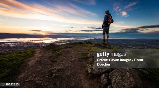 man hiker standing on rock overlooking san francisco bay at sunset - bucht-von-san-francisco stock-fotos und bilder
