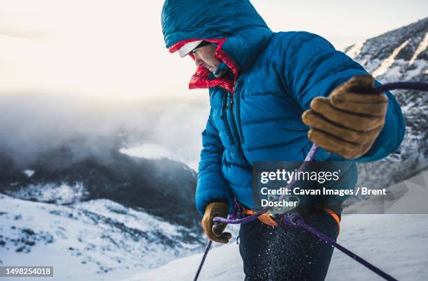male climber belays his lead climber during a cold winter alpine climb - zekeren stockfoto's en -beelden