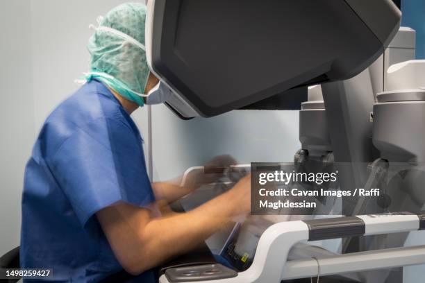 a surgeon manipulates the controls of a robot that operates a patient - robotic surgery stock pictures, royalty-free photos & images