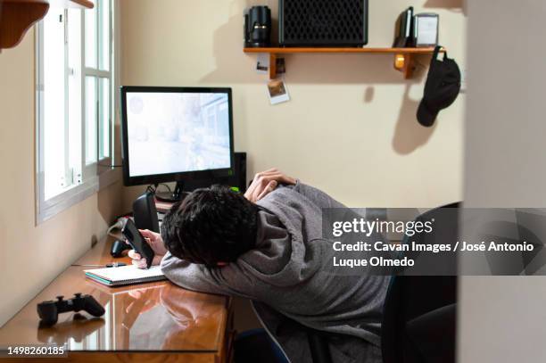 bored man using a phone in a room full of technology during a long day - perder el tiempo fotografías e imágenes de stock