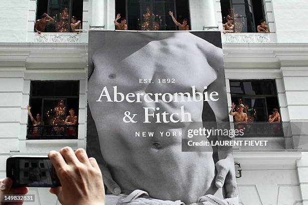 Man uses his mobile phone to take photographs of topless male models waving to a crowd of onlookers from the soon to open Abercrombie & Fitch...