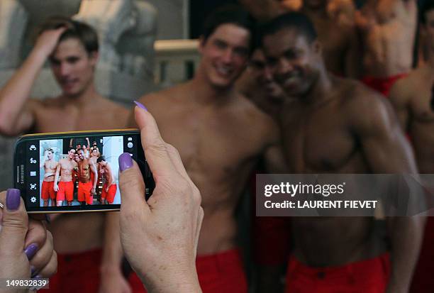 Woman uses her mobile phone to take photographs of a group of topless male models outside the soon to open Abercrombie & Fitch flagship clothing...
