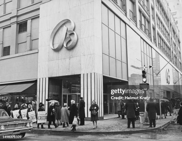 Striking shopworkers wearing sandwich boards reading 'Employees of Bloomingdale's on Strike' form a picket line on the sidewalk outside...