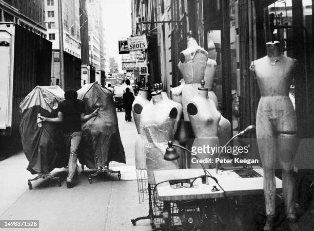Man pulling two clothes rails alongside mannequins outside clothing stores on West 35th Street in the Garment District in the borough of Manhattan,...