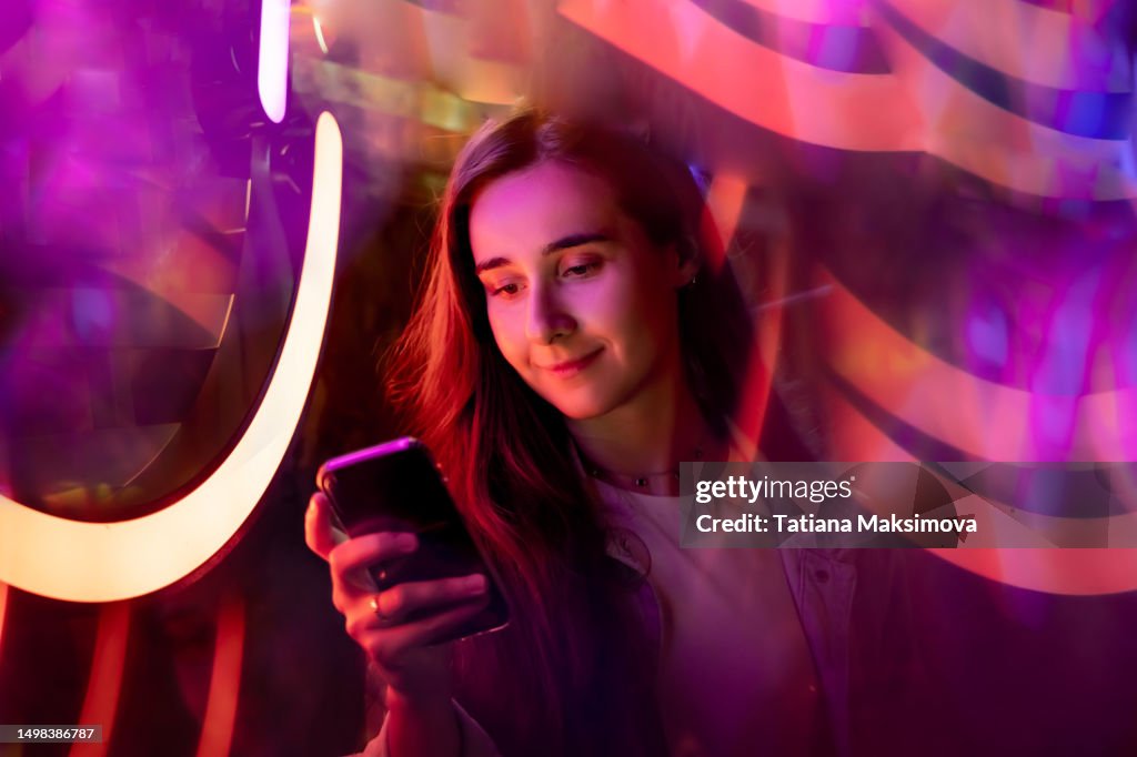 Young beautiful woman with mobile phone on neon background.