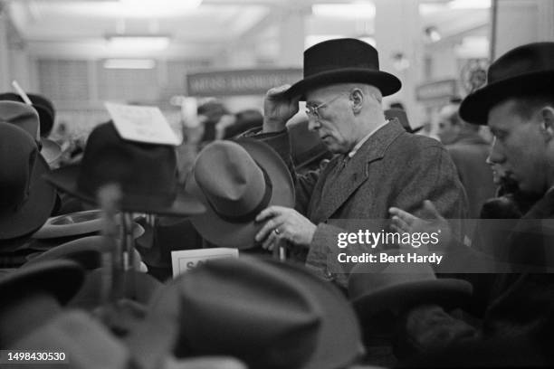 Men trying on hats in a department store during the winter sales, Britain, January 1950. Original Publication: Picture Post - 4966 - Women Into...