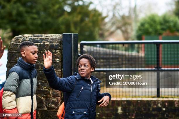 two boys approaching school gates, one waving - school building stock pictures, royalty-free photos & images