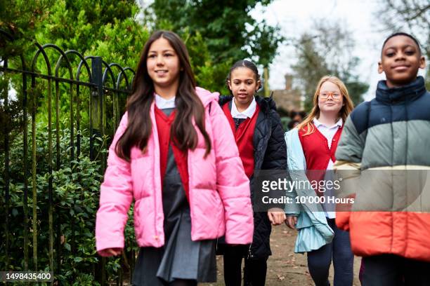 group of children walking to school wearing coats and smiling - school uk stock pictures, royalty-free photos & images