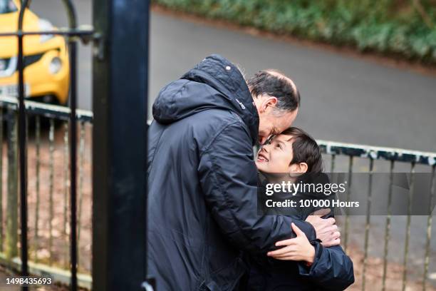 father and son in affectionate embrace outside school gates - school gates stock-fotos und bilder