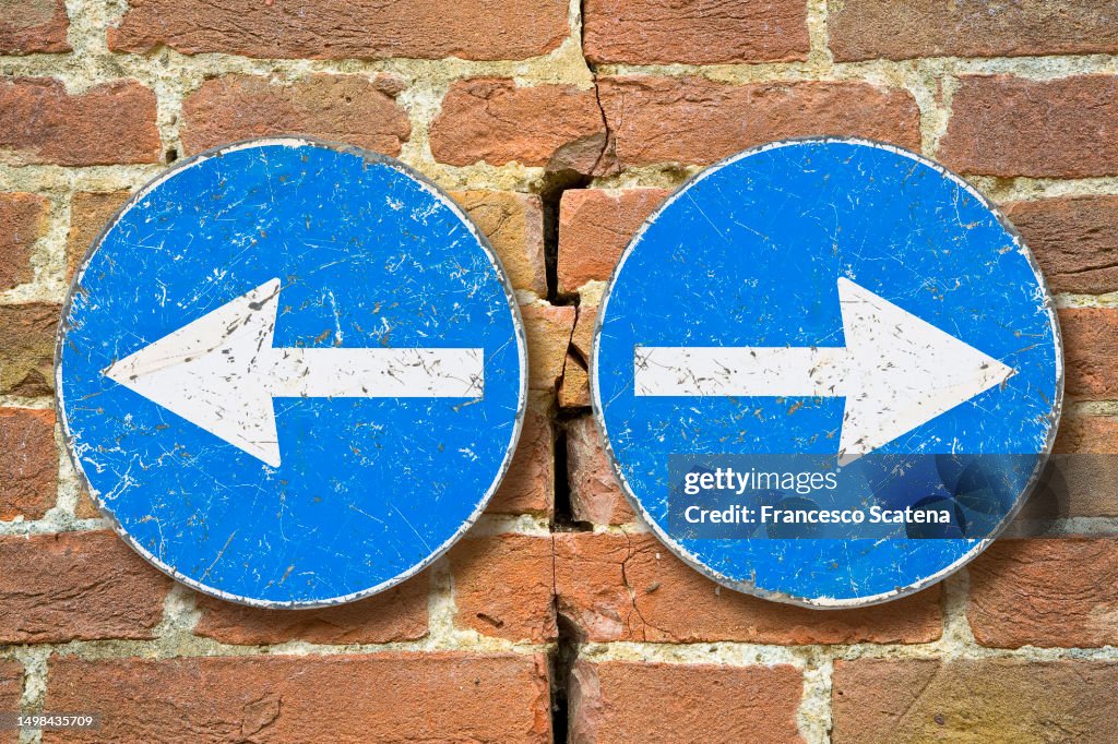 Old blue metallic arrow sign against an aged cracked brick wall indicating to go left and right - concept image