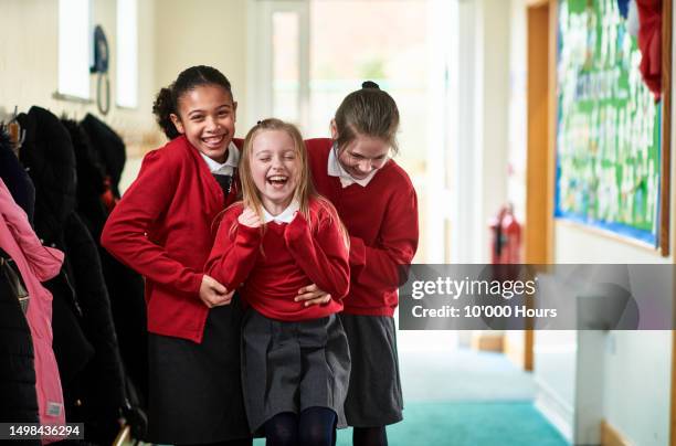 two girls tickling friend in school cloakroom - veralbern stock-fotos und bilder