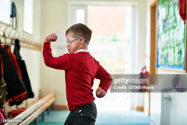boy with down syndrome flexing muscles in school corridor - disabilitycollection fotografías e imágenes de stock
