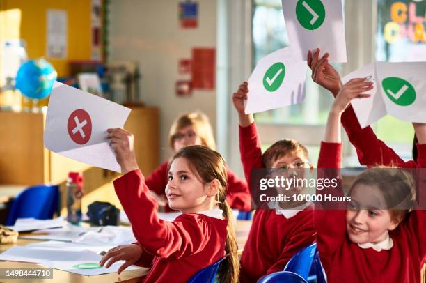 boy with down syndrome in class holding up piece of paper with green tick - class argument stockfoto's en -beelden