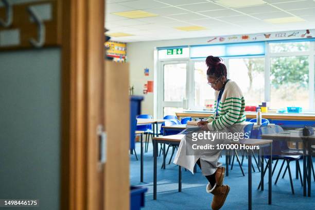 mid adult female teacher sitting on desk with classroom door open - open day 10 stock-fotos und bilder