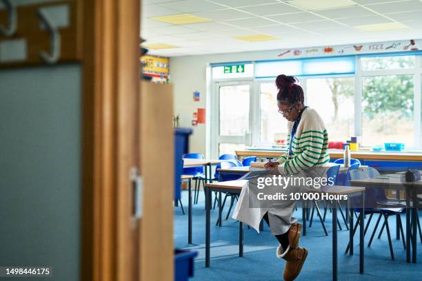 mid adult female teacher sitting on desk with classroom door open - open day 10 stockfoto's en -beelden