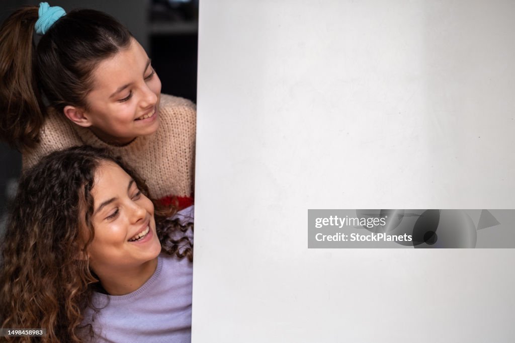 Two teenage girls are smiling and looking at the white background