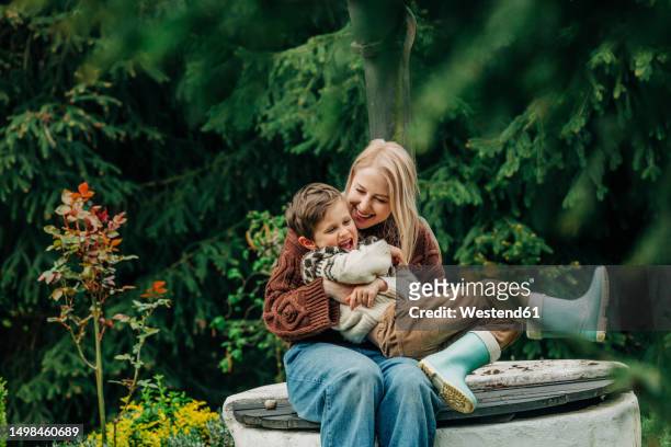 mother with son sitting together on well in garden - tickling stock-fotos und bilder