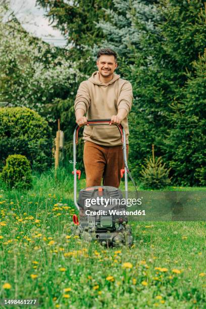 smiling man standing with lawnmower in garden - mowing stock pictures, royalty-free photos & images