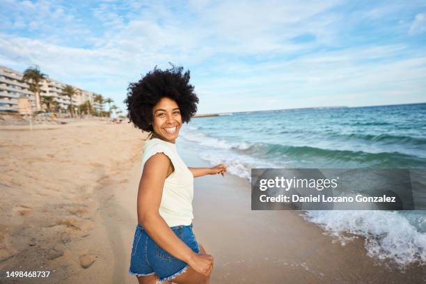 woman turning smiling at camera while running along the beach - african american women in the wind photos et images de collection