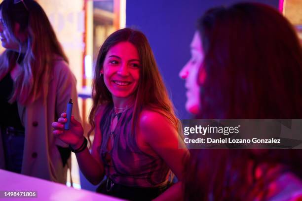 woman sitting in a disco with an electronic cigarette - world health organisation calls for regulation of ecigarettes stockfoto's en -beelden