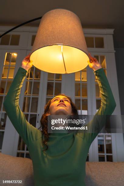 young woman adjusting illuminated lamp at home - adjusting stock pictures, royalty-free photos & images
