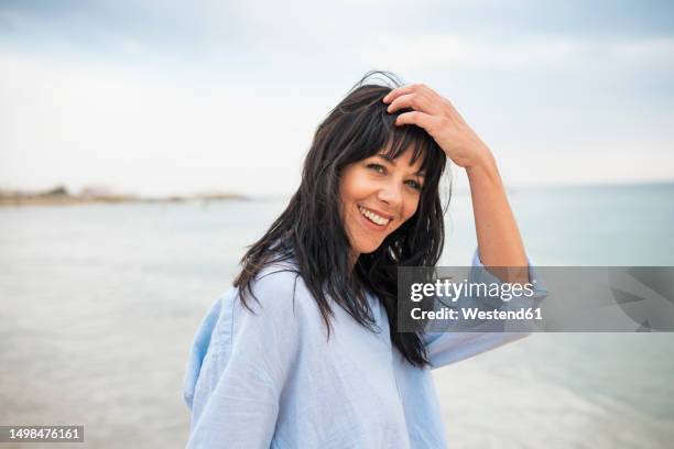 smiling woman with hand in hair at beach - 髪に手をやる　女性 ストックフォトと画像