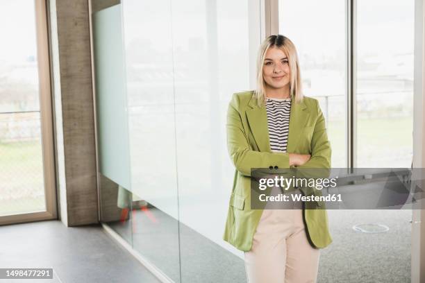 confident businesswoman with arms crossed standing by glass door in office - green blazer stock pictures, royalty-free photos & images