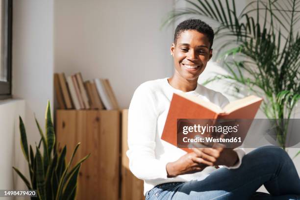 smiling woman reading book at home - literature concept stock pictures, royalty-free photos & images