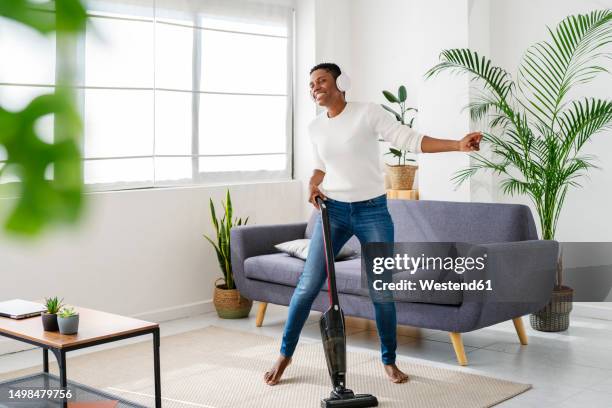 carefree woman vacuum-cleaning and listening to music with headphones at home - house cleaning stock pictures, royalty-free photos & images