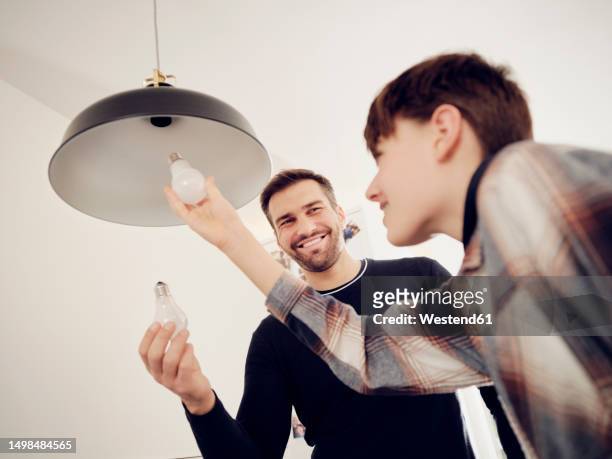 son and father changing old lightbulb for a led energy saving lightbulb - bombilla de bajo consumo fotografías e imágenes de stock