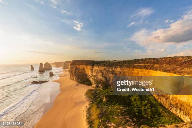 australia, victoria, view of sandy beach in port campbell national park at sunset with twelve apostles in background - twelve apostles stock pictures, royalty-free photos & images