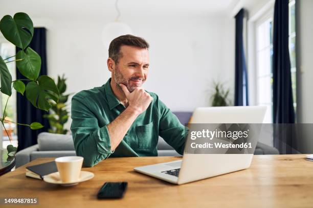 mature businessman working from home using laptop - grünes hemd stock-fotos und bilder
