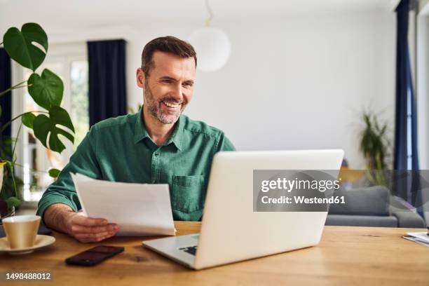 confident businessman doing paperwork sitting at table working from home - grünes hemd stock-fotos und bilder