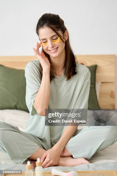 vertical shot of a young woman performing her beauty routine in the morning while sitting up in bed - augen schönheit creme stock-fotos und bilder