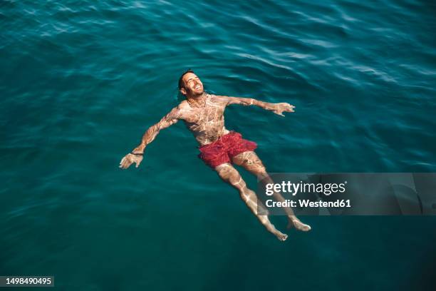 carefree young man swimming in sea at vacation - auf dem wasser treiben stock-fotos und bilder