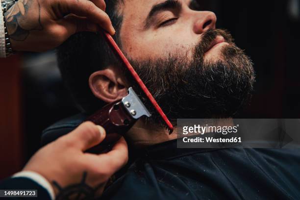 customer with eyes closed getting beard trimmed in barber shop - beard trimmer stock pictures, royalty-free photos & images