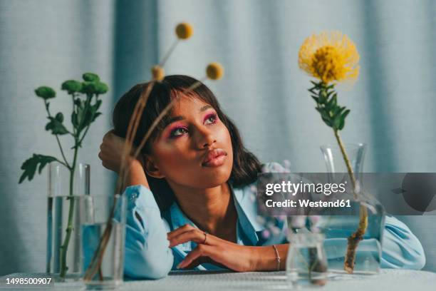 thoughtful woman sitting at table with flowers in front of blue backdrop - bangs stock pictures, royalty-free photos & images