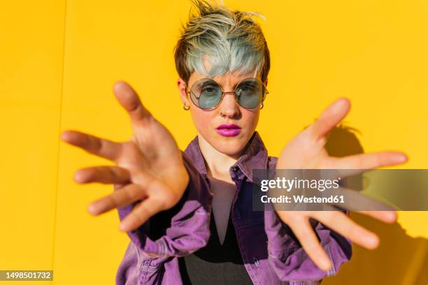 woman wearing sunglasses showing palms in front of yellow wall - rossetto rosa foto e immagini stock