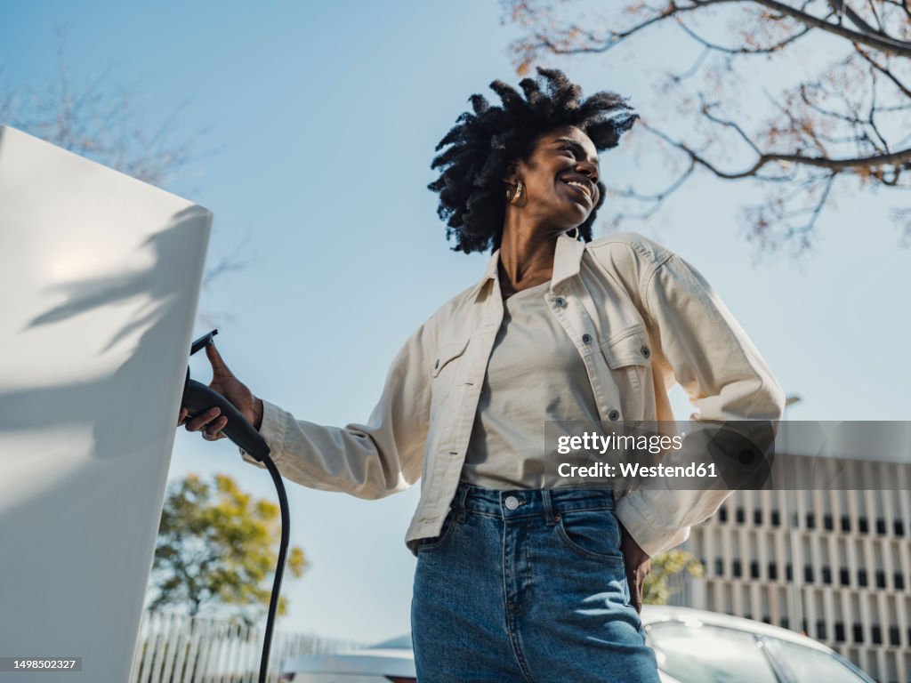 Smiling young woman charging electric car