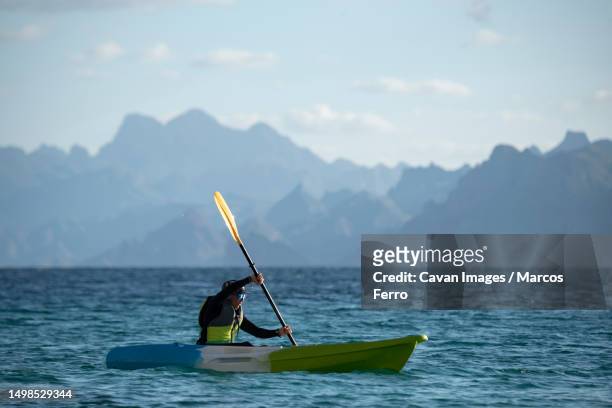 one woman paddling on a seat on top kayak close to the shore of carmen island in loreto, baja california, mexico - sea kayaking imagens e fotografias de stock