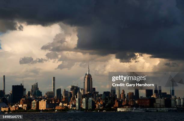 The sun sets on the skyline of midtown Manhattan and the Empire State Building as storm clouds pass over New York City on June 14 as seen from Jersey...